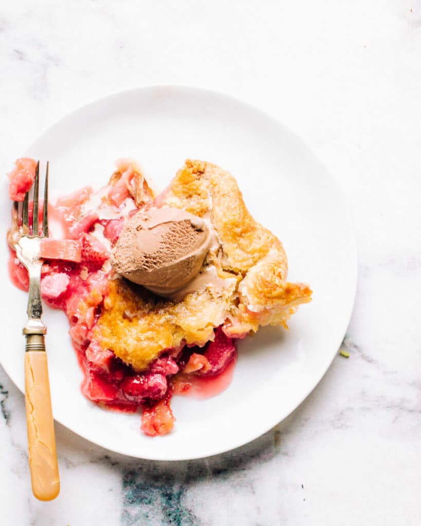 strawberry rhubarb pie on a plate with ice cream.
