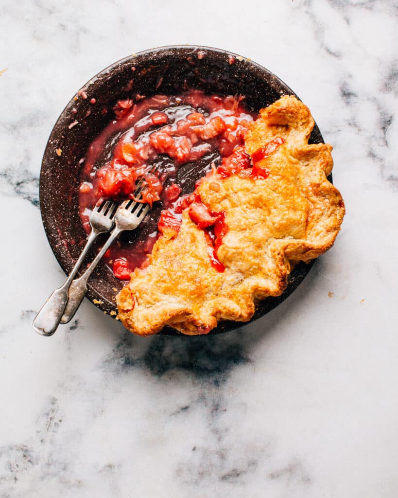 Strawberry rhubarb pie in a pie plate with two forks.