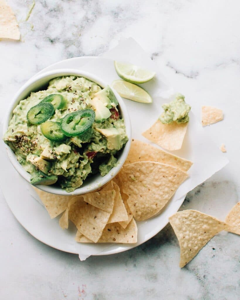 Authentic mexican guacamole in a bowl with jalapenos on top.