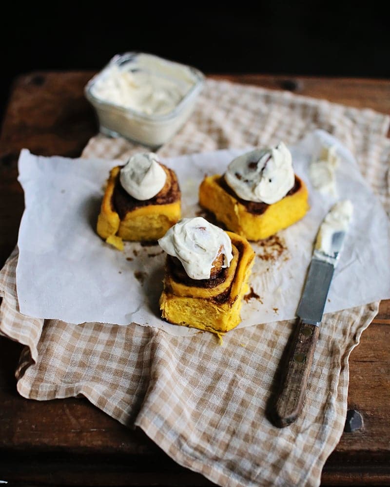 pumpkin cinnamon buns with cream cheese frosting on a brown checkered dish towel