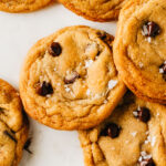 Chewy Chocolate Chip cookies sprinkled with salt on a parchment-paper background.