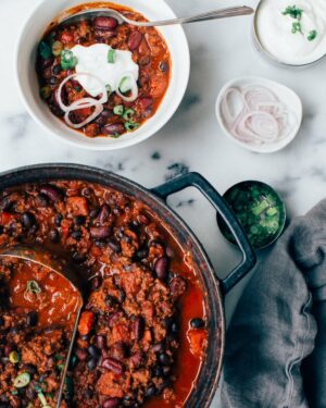Ground beef chili in a pot with a bowl of chili next to it.