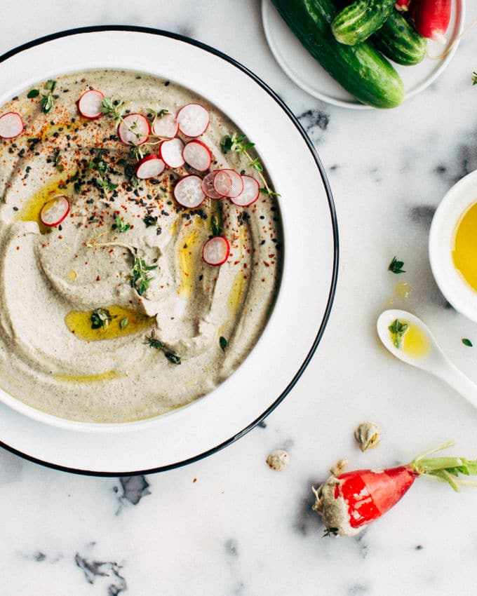 Hummus is presented in a bowl, garnished with sliced radish and sesame seeds.