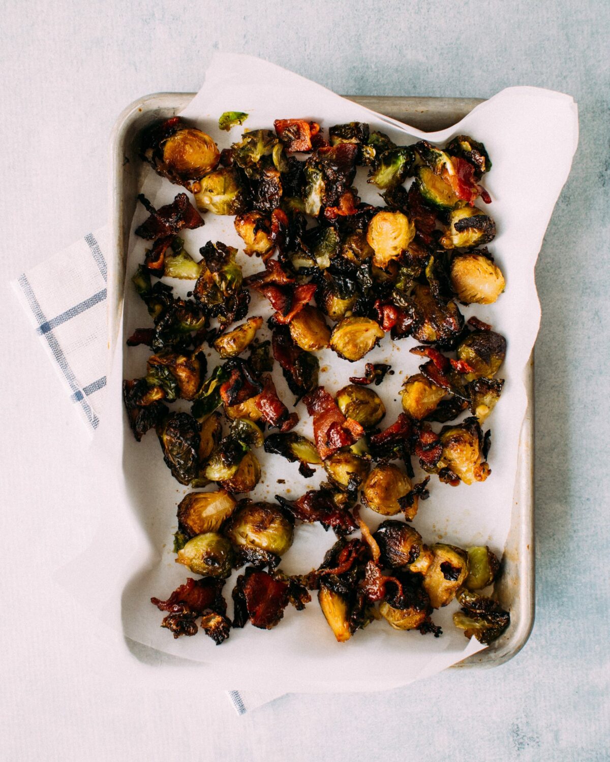 Baked roasted maple bacon brussels sprouts on parchment-lined baking sheet, on a tea towel.