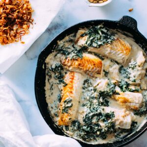 A skillet with fish in tahini sauce.