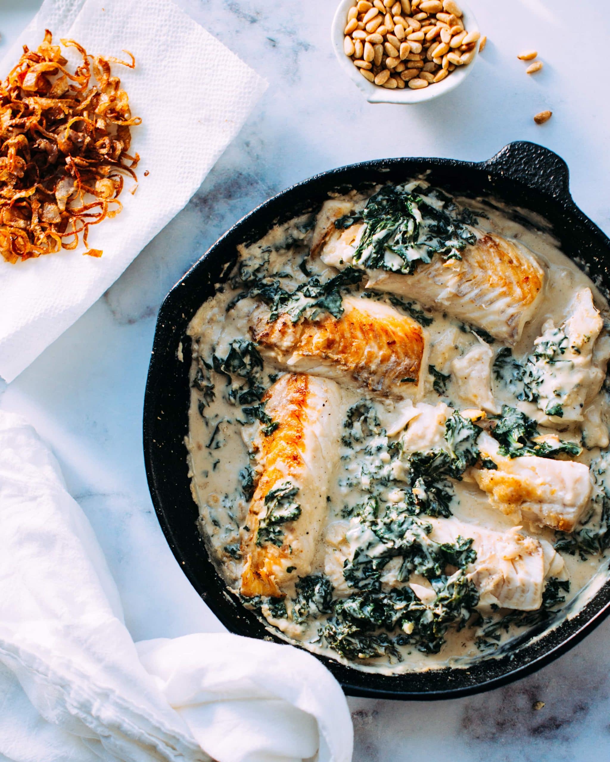 A skillet with fish in tahini sauce.