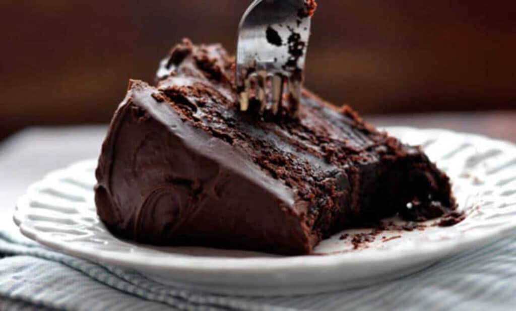 A slice of moist chocolate cake on a plate with a fork.