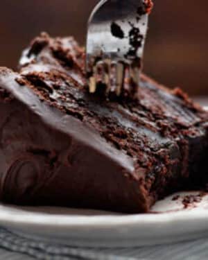 A slice of moist chocolate cake on a plate with a fork.
