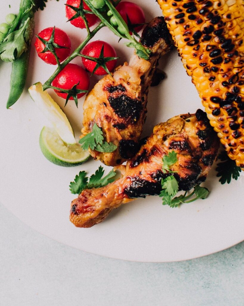 Garlic & Lime Grilled Chicken on a plate with corn cob, baby tomatoes and sliced lime wedges