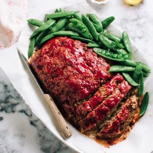 The best meatloaf, sliced on a plate with snap peas.