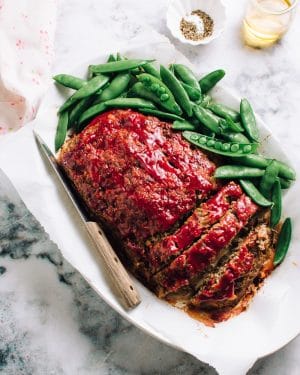 The best meatloaf, sliced on a plate with snap peas.