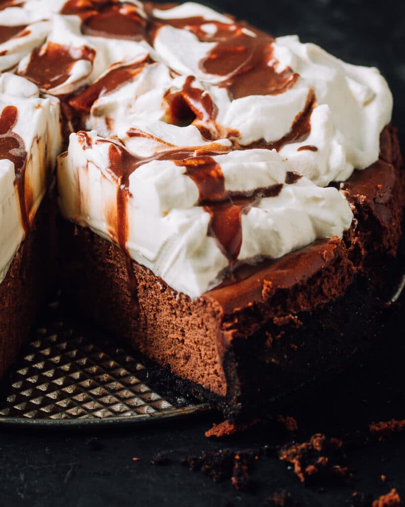 Chocolate cheesecake with whipped cream and chocolate drizzle with a slice cut.