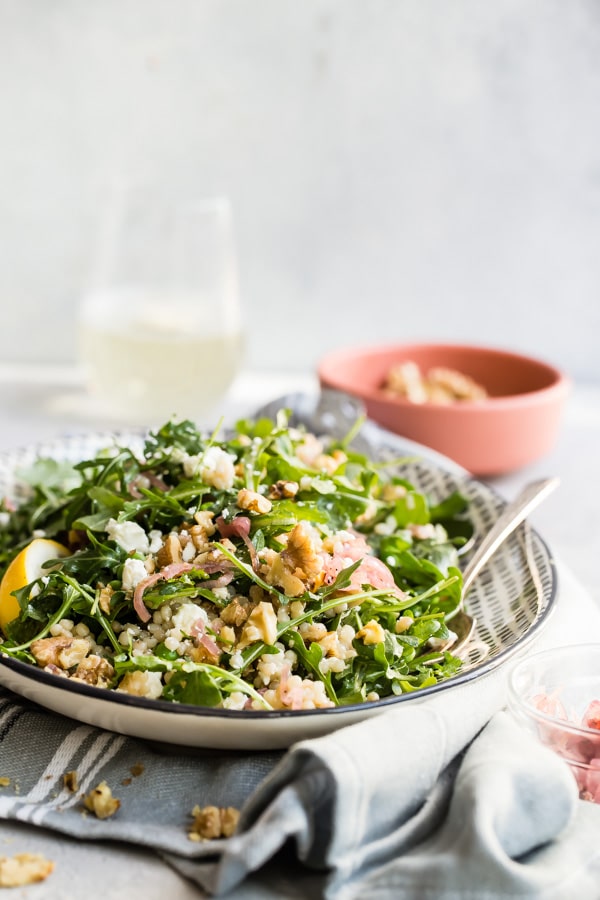 Israeli couscous salad with arugula and walnuts on a plate.