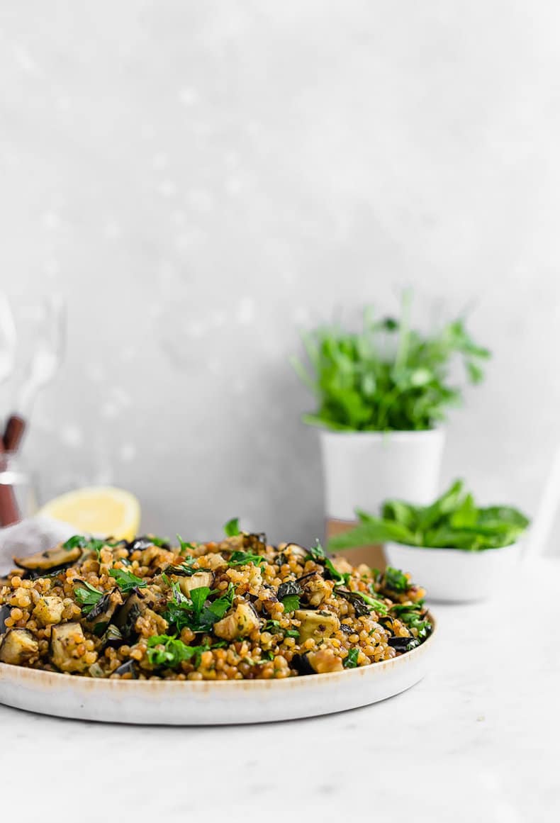 Israeli couscous salad with eggplant and herbs on a plate.
