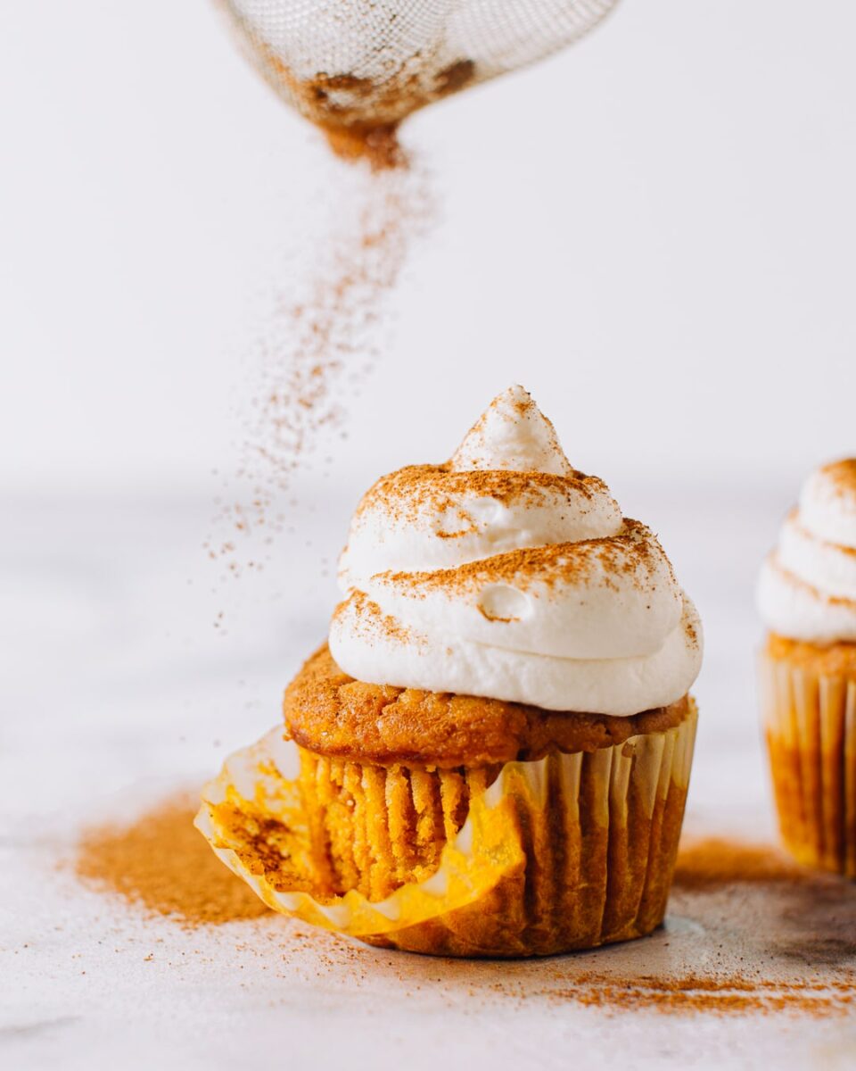 Pumpkin cupcake being dusted with cinnamon.