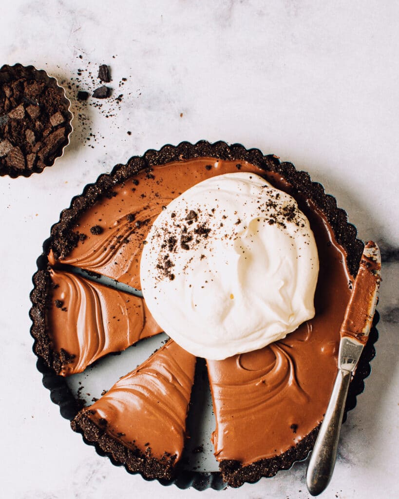 A chocolate tart cut into slices with whipped cream on top