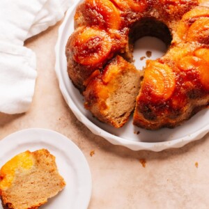 A slice of peach cobbler pound cake on a plate beside whole cake.