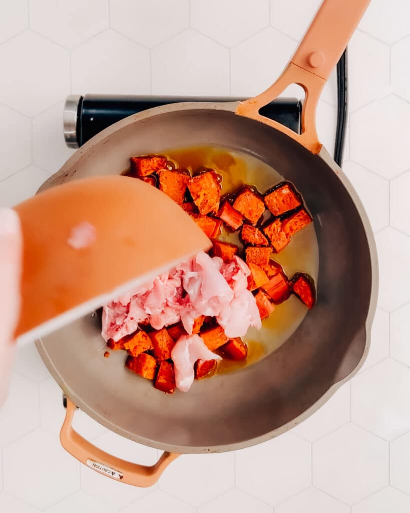 Adding chicken and chorizo to hot oil in a frying pan.