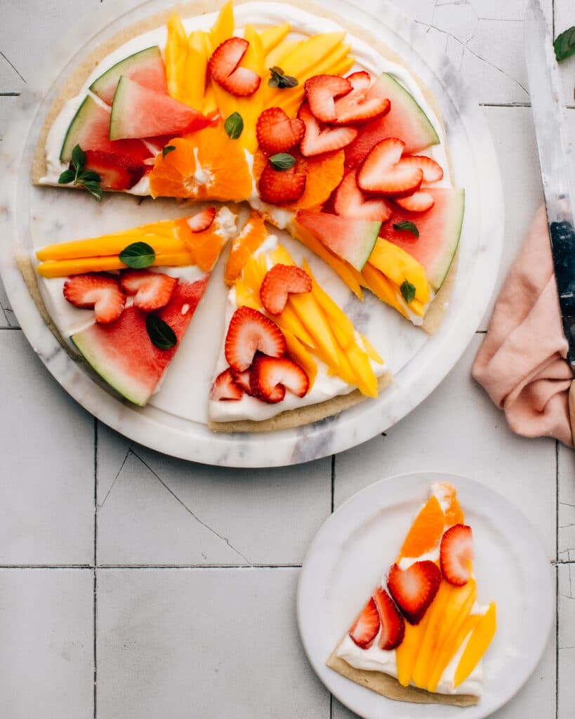 This Fruit Pizza recipe has the best, fluffy cream cheese frosting and an easy sugar cookie base.  You can make fun, beautiful fruit designs into Easter eggs, a patriotic flag for Memorial Day or Canada Day, or any holiday.
