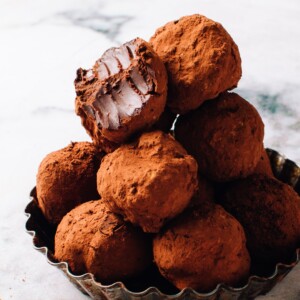 A pile of chocolate truffles in a dish with a bite out of one.