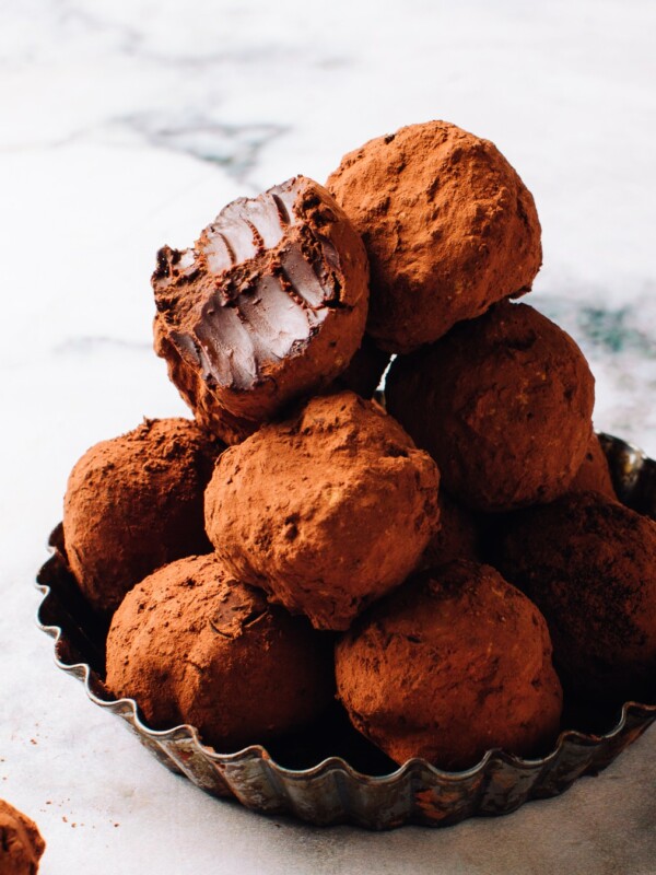 A pile of chocolate truffles in a dish with a bite out of one.