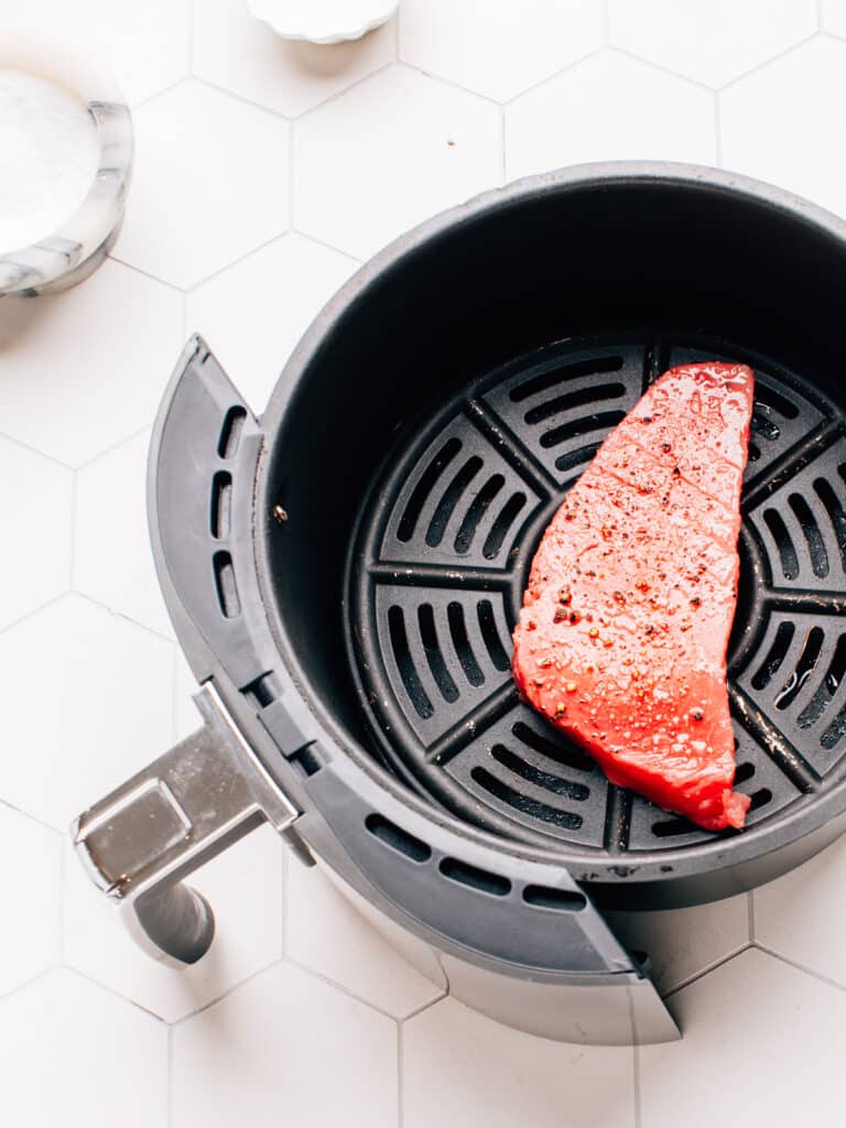 Raw ahi tuna steak in the air fryer basket with salt and pepper.