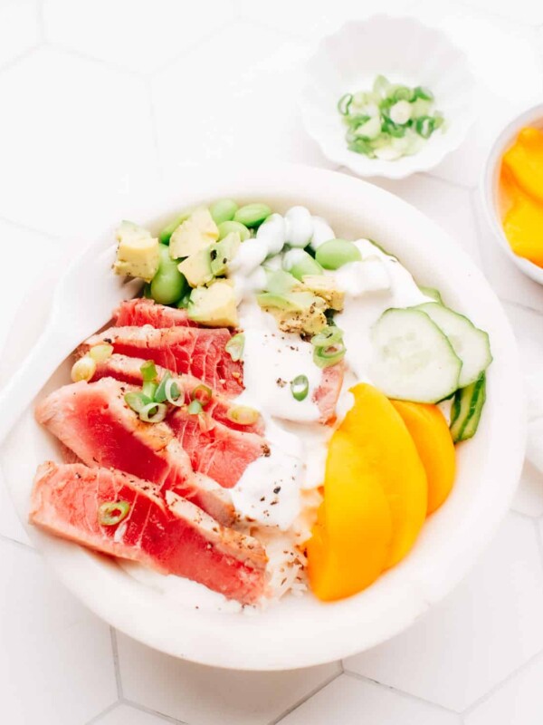Sliced seared air fryer tuna in a poke bowl with peach slices, edamame, cucumber and green onions, drizzled with sauce.