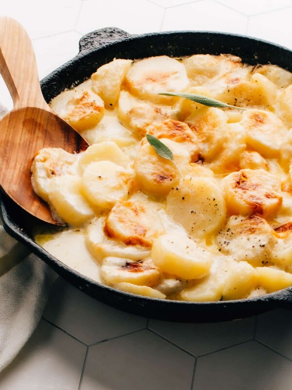 Gluten-free potatoes au gratin in a cast iron pan with serving spoon.