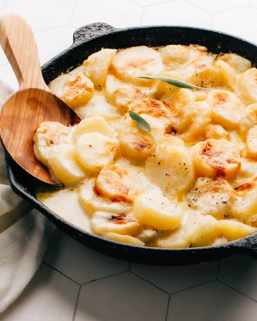 Gluten-free potatoes au gratin in a cast iron pan with serving spoon.