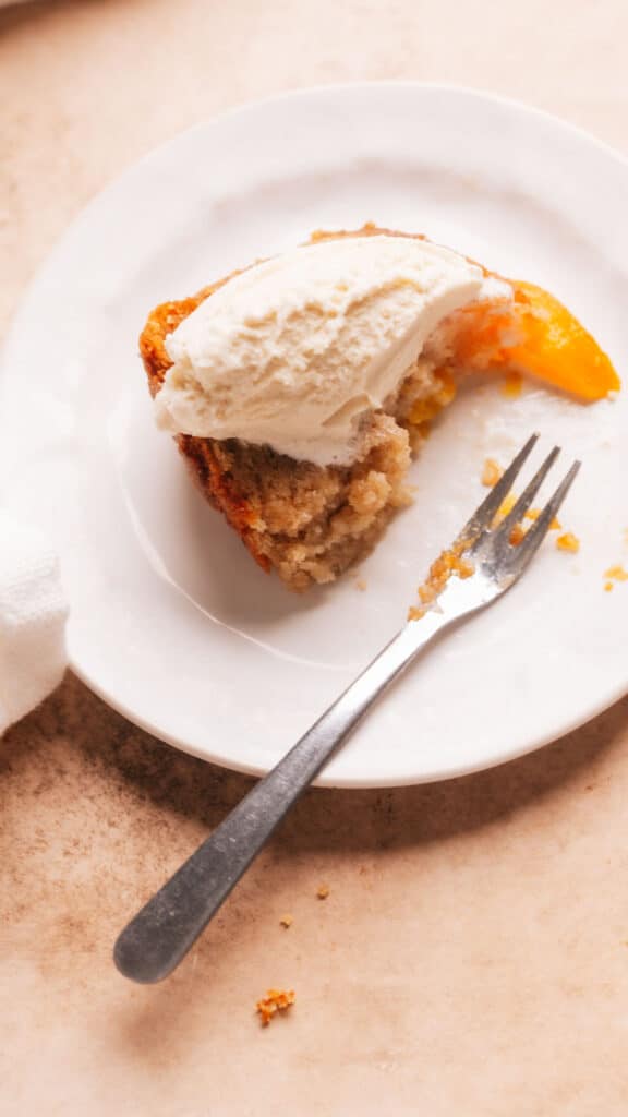 A slice of peach cobbler pound cake with ice cream on a plate with a fork.