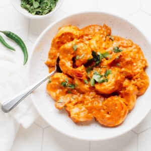A serving bowl with shrimp korma with cilantro on top and a bowl of cilantro on the side.