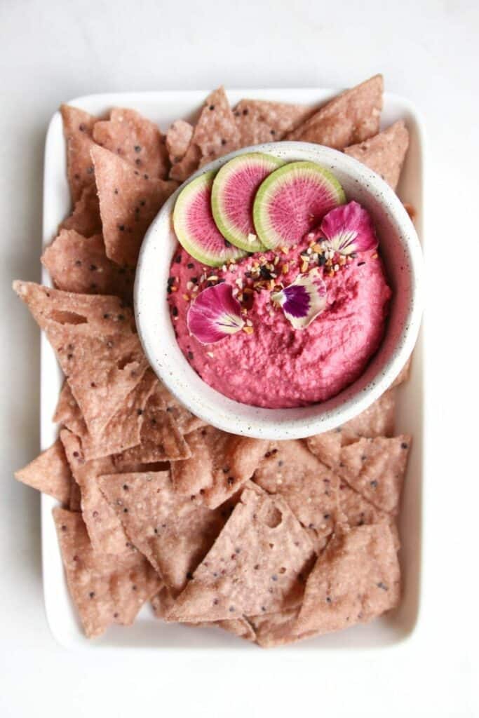 Bowl of garlic beet hummus served with crunchy potato chips for dipping