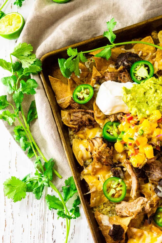 Half side view of delicious Sheet Pan Jerk Pork Nachos with melted cheese and colourful toppings
