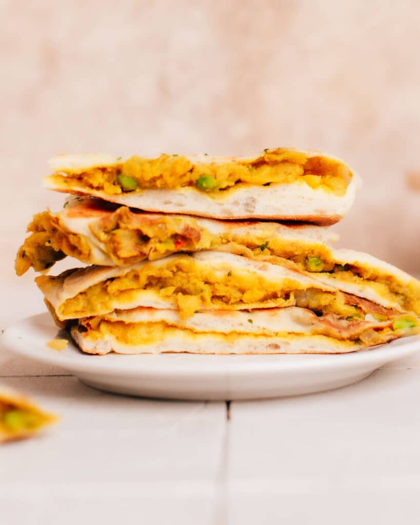 Side view of a half-cut aloo naans with visible filling, stacked on a plate.
