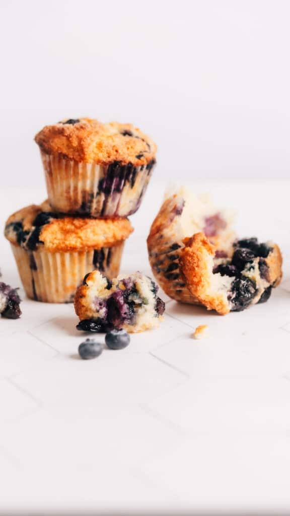 Stack of lemon blueberry sour cream muffins with one muffin halved on a table