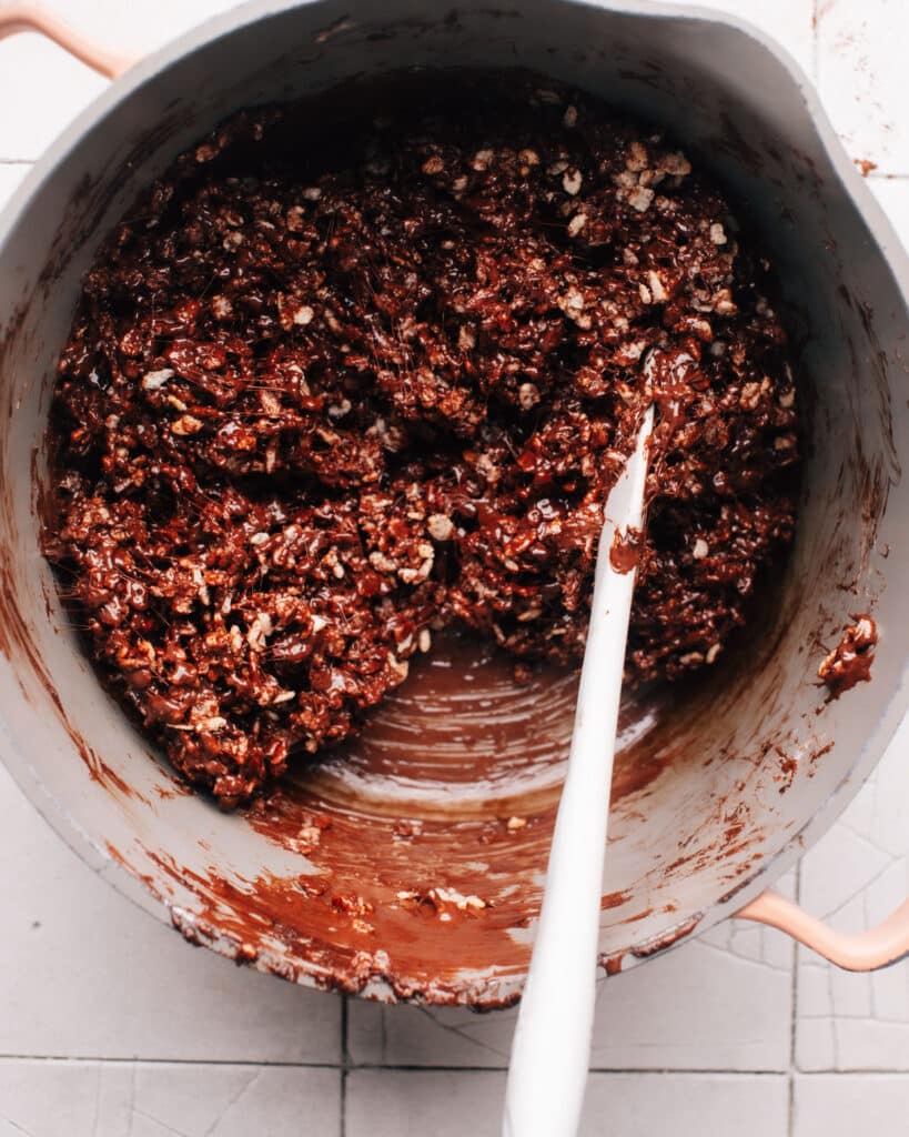 A saucepan filled with melted marshmallows, chocolate chips, and rice krispie cereal mixture ready to be poured into a baking sheet.