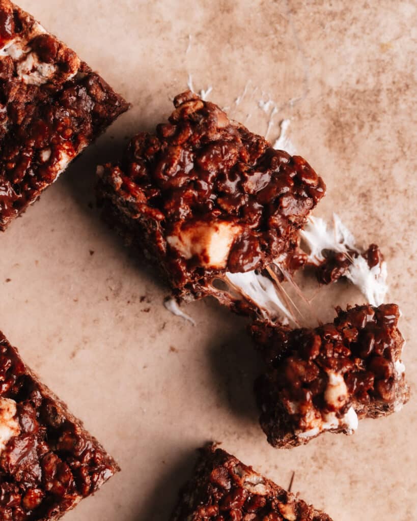 Chocolate rice krispie treat cut into 2 pieces, revealing the gooey melted marshmallows and chocolate chips in its texture.