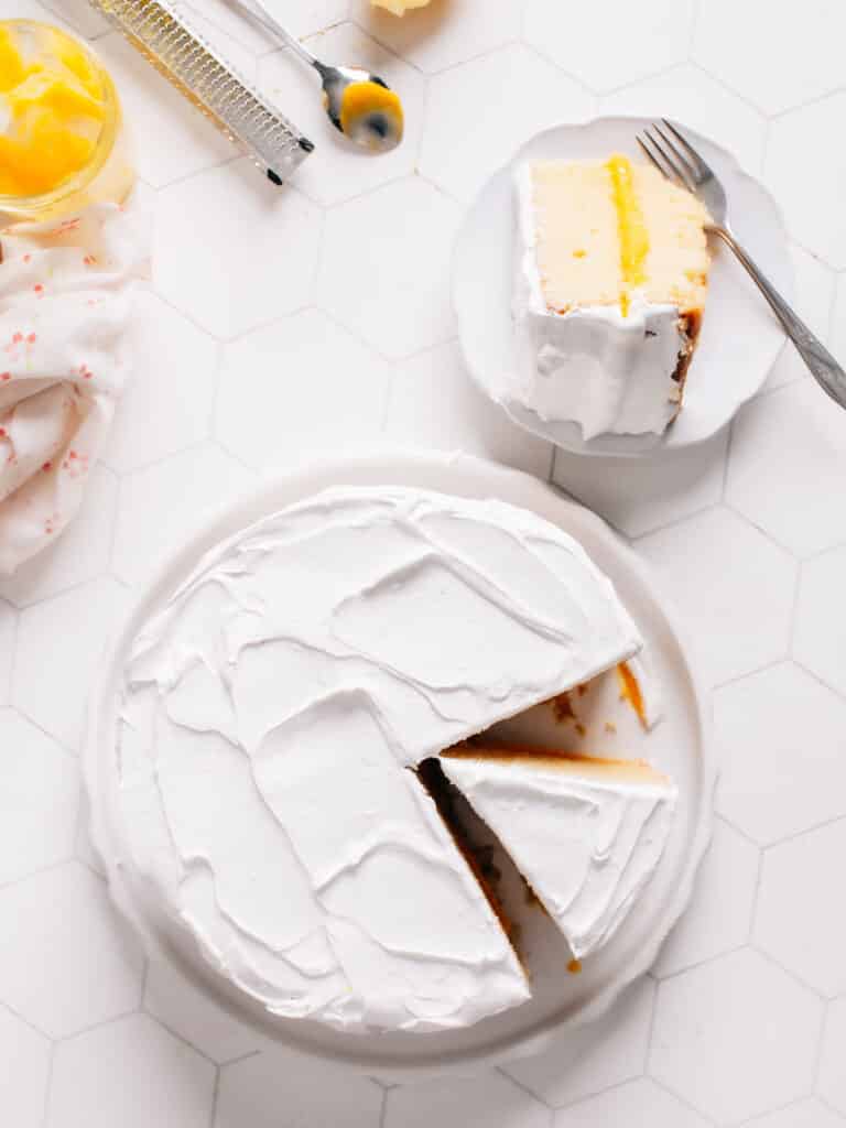 A scrumptious lemon curd cake has been sliced and plated on a white dish with a fork by side.