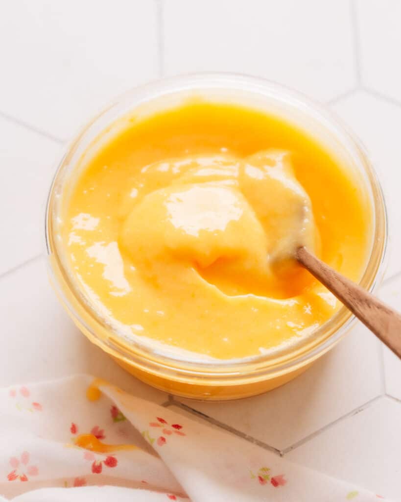 Fresh lemon curd filling in a small cup with a wooden spoon inside