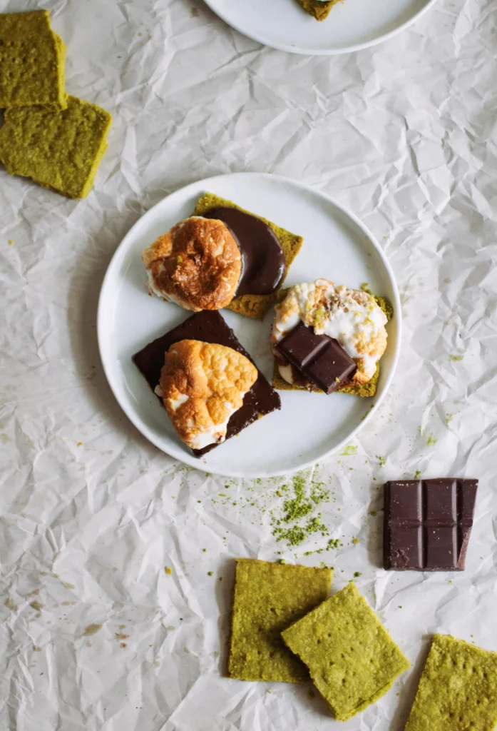 Matcha shortbread cookies topped with s'mores and melted chocolate on a white plate