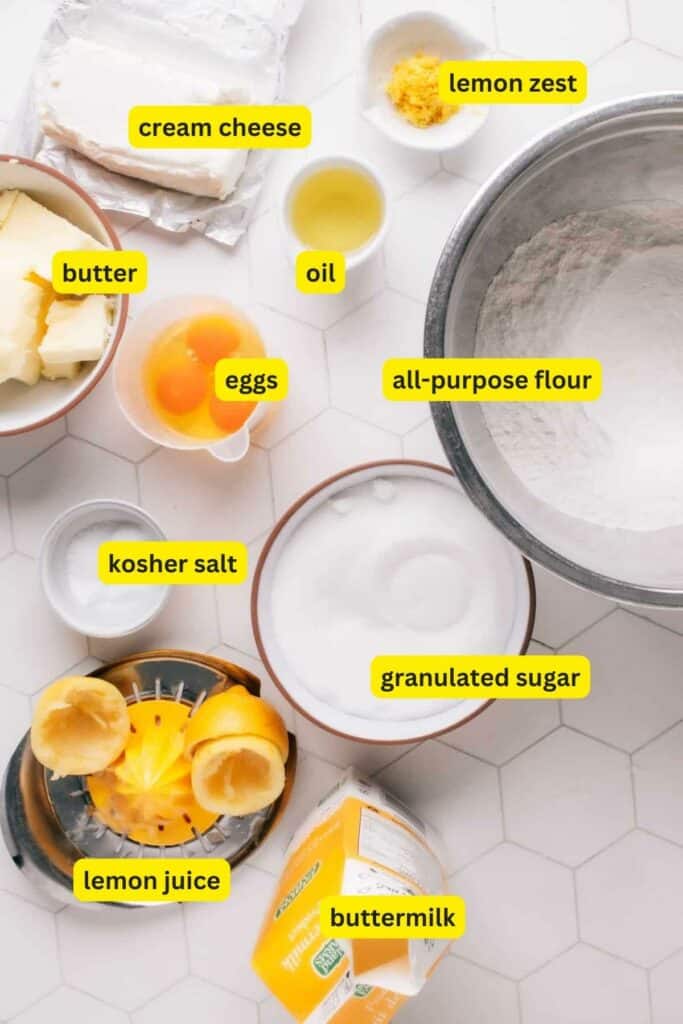 Ingredients for Lemon Curd Cake laid out on a kitchen countertop including all-purpose flour, eggs, cream cheese, lemon, butter, oil, sugar, buttermilk, etc.