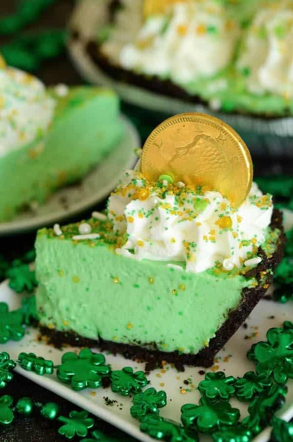 A slice of no-bake shamrock freezer pie with whipped cream and a chocolate gold coin on top, perfect for St. Patrick's Day