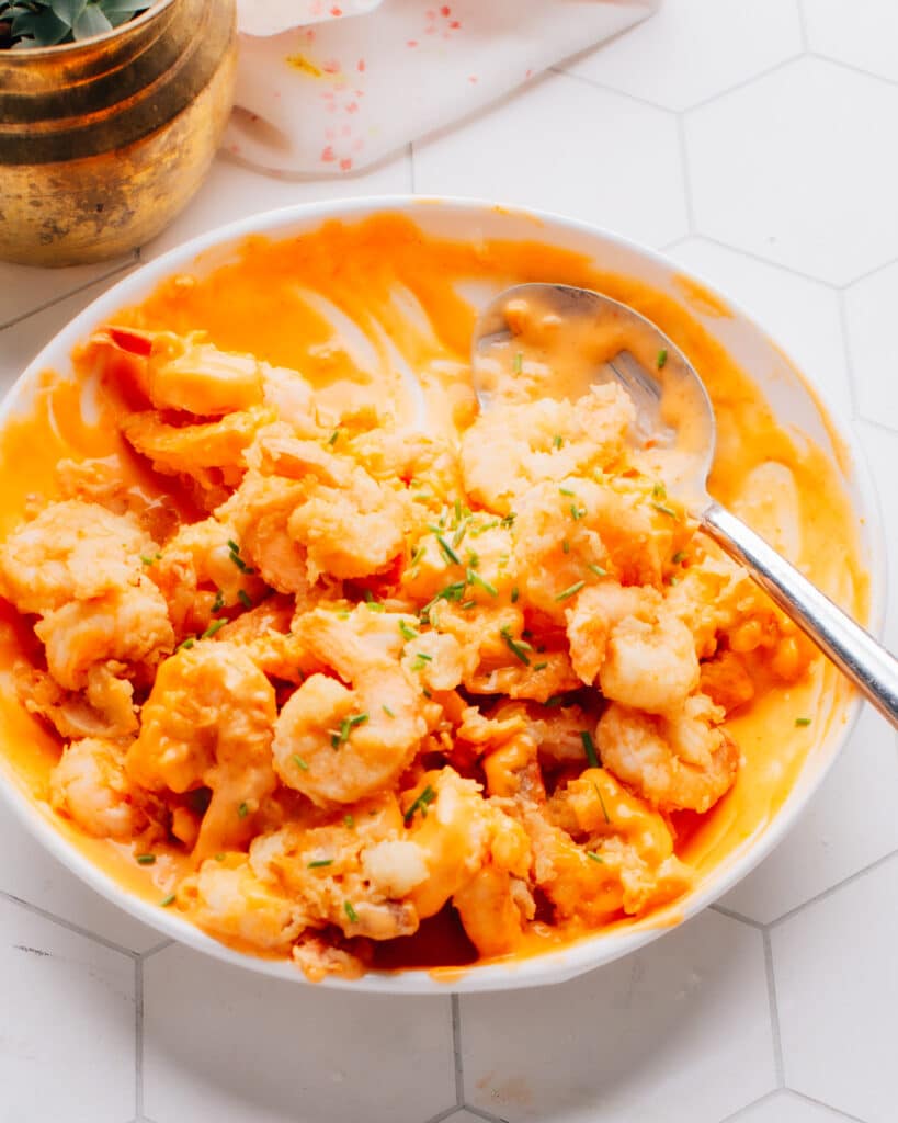 A medium white bowl containing Boom Boom Shrimp, which is a crispy and spicy shrimp dish coated with a creamy sauce.