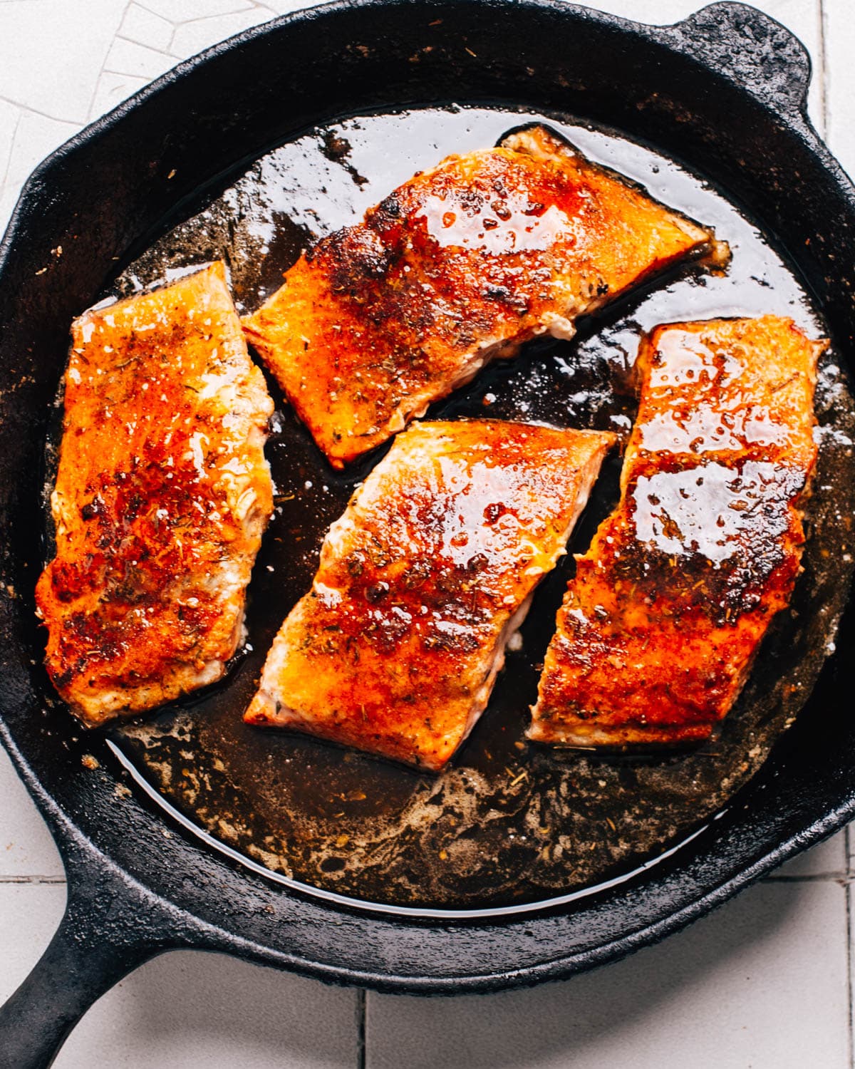 A cast iron skillet contains 4 salmon fillets that have been seasoned with Cajun spices and brushed with honey butter.