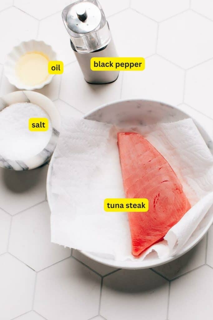 Ingredients for Air Fryer Tuna Steak arranged on a kitchen countertop, including tuna steak, salt, black pepper, and oil.