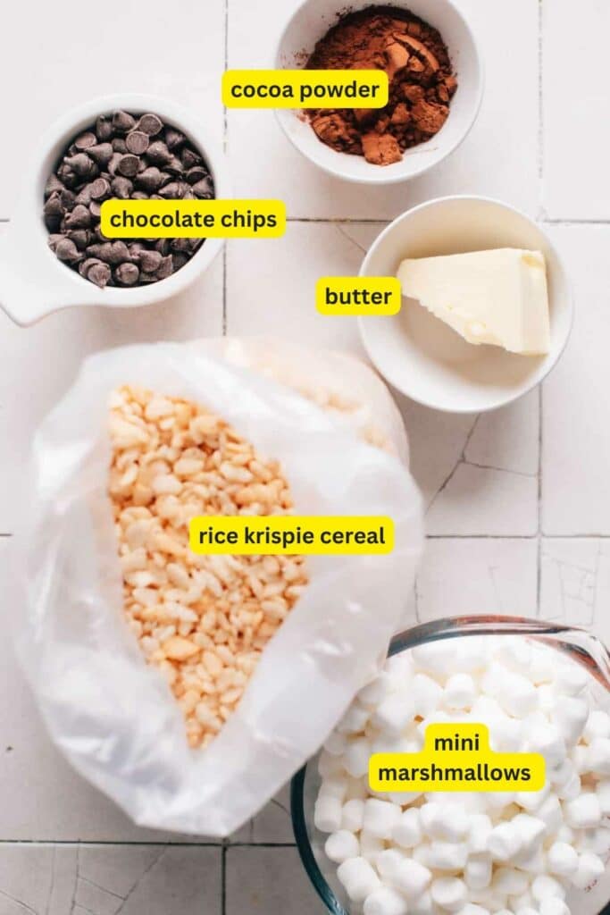 Ingredients for Chocolate Rice Krispie Treats laid out on a kitchen countertop, including, cocoa powder, chocolate chips, butter, mini marshmallows and rice krispie cereal.
