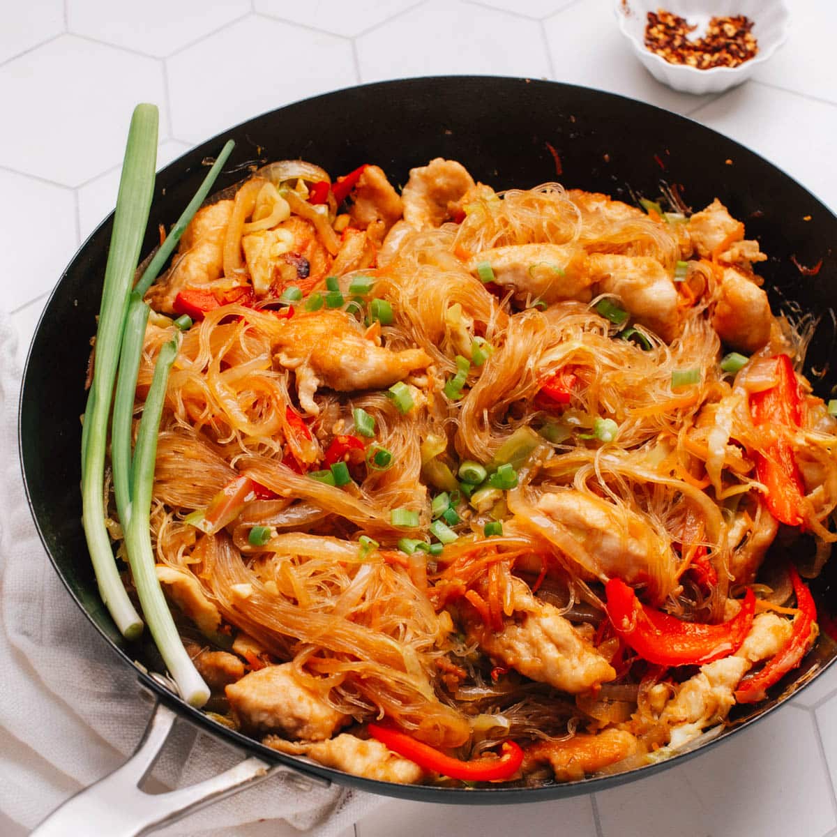 Pad Woon Sen (Thai Glass Noodle Stir Fry) is presented in a skillet, with a garnish of green onions on top.