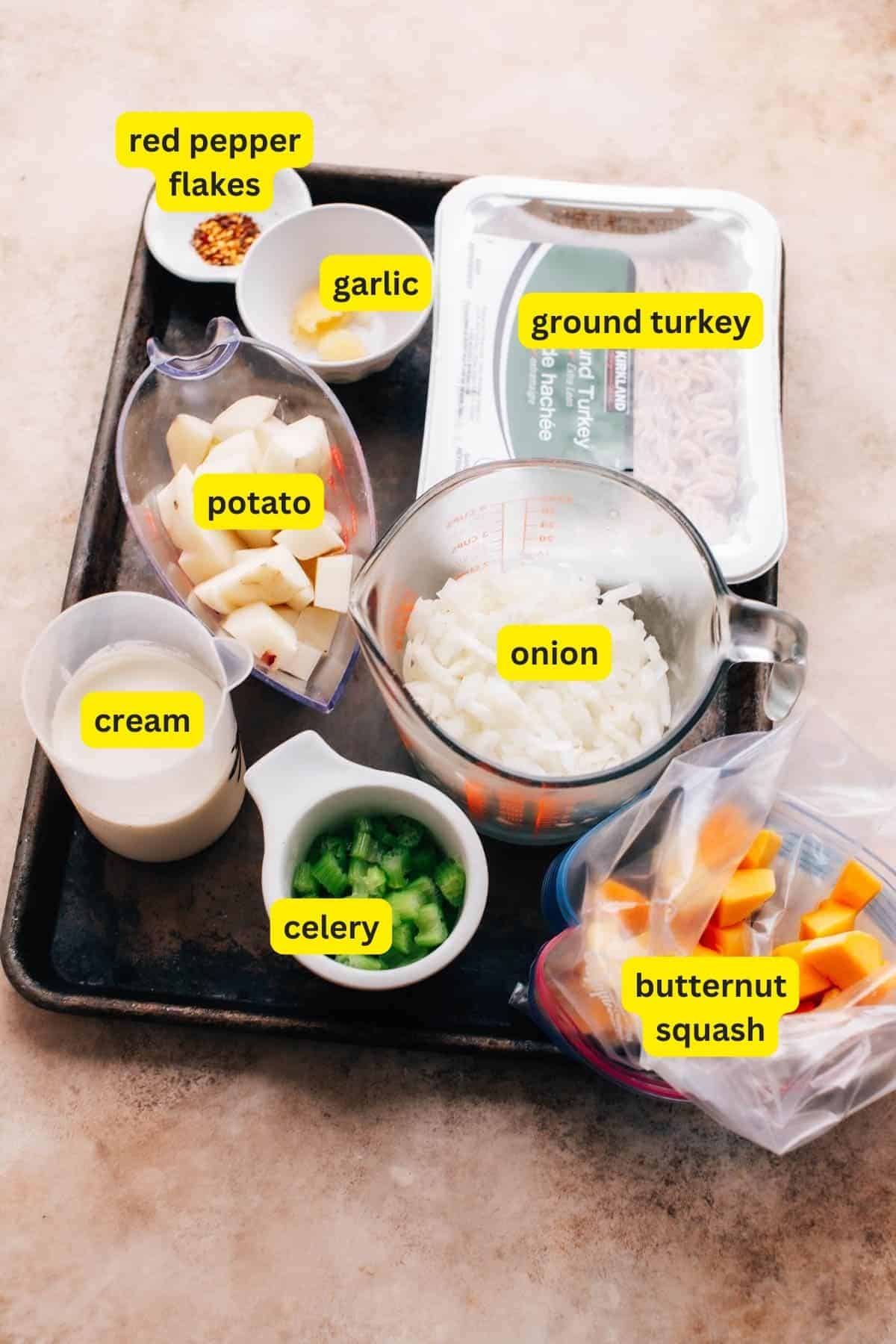 Ingredients for ground turkey soup are laid out on a kitchen countertop including celery, ground turkey, onion, minced garlic, red pepper flakes, potato, butternut squash and cream.