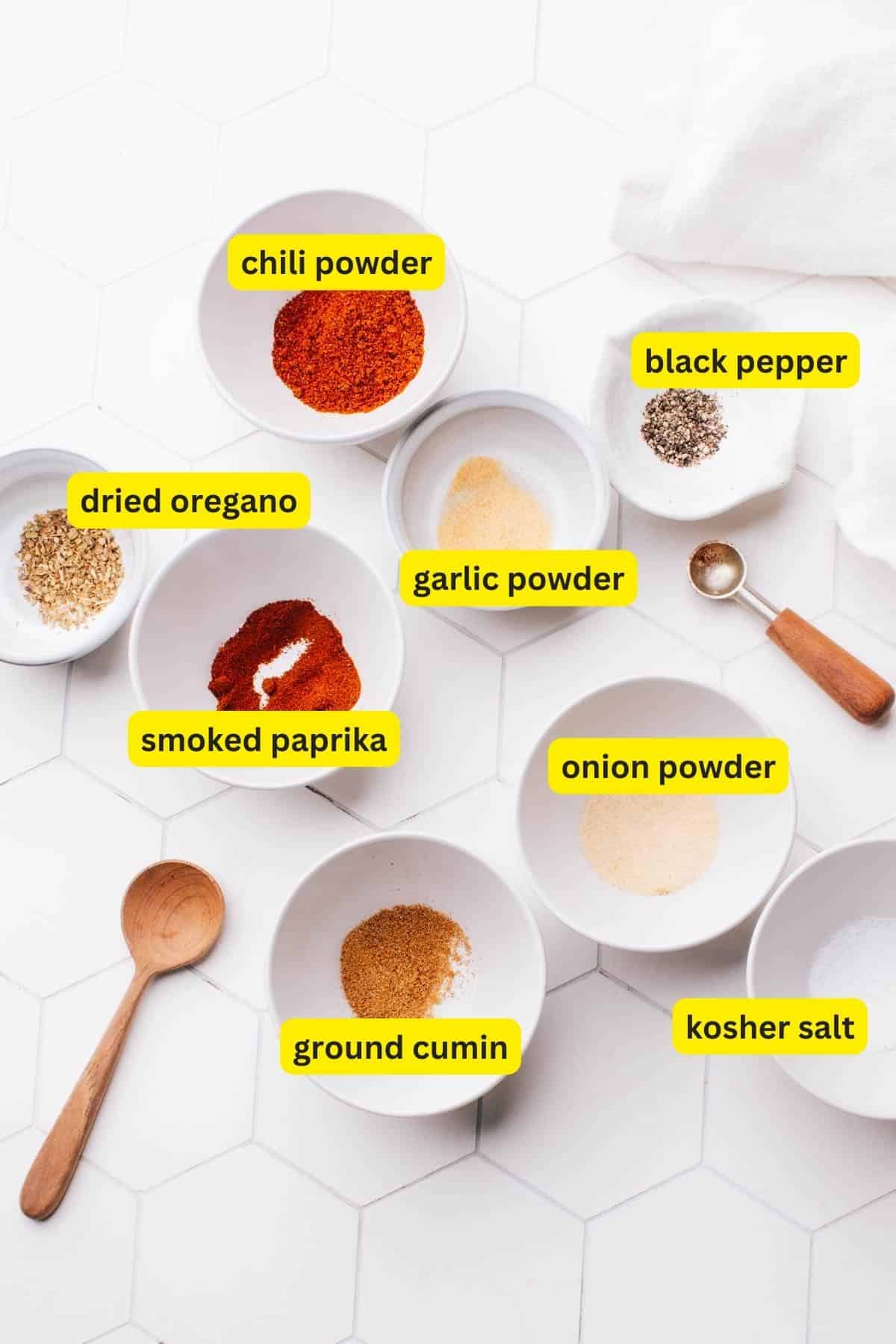 Ingredients for chicken taco seasoning laid out on a kitchen countertop, including chili powder, black pepper, dried oregano, garlic powder, smoked paprika, onion powder, ground cumin and kosher salt.