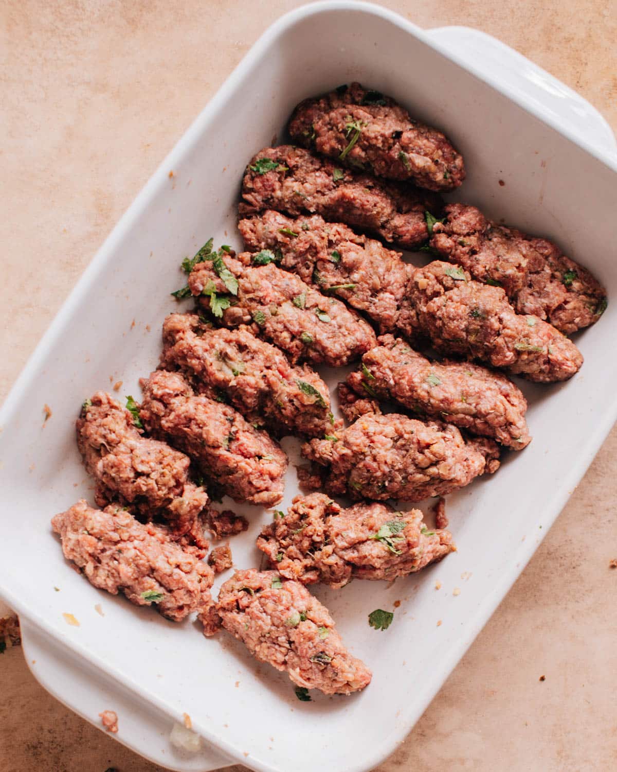 A white dish with long sausage-like shapes formed from the beef kafta kabob mixture.